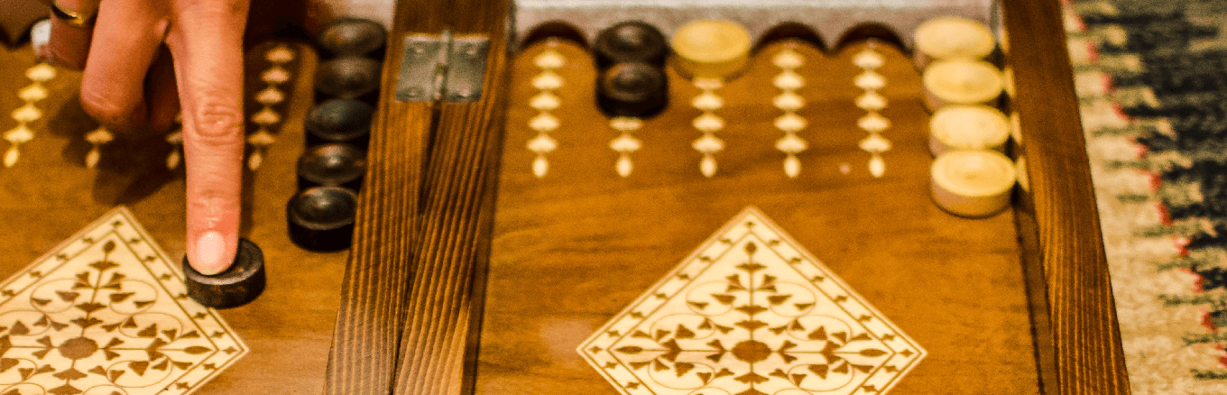 Hand moving a backgammon chip on a backgammon table.