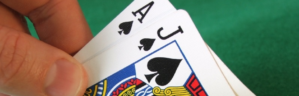 A hand holding an Ace (A) and a Jack (J) cards on a blackjack table, representing the potential for a strong hand in the game